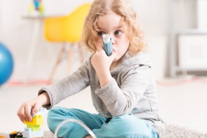 Cropped shot of a small girl sitting on a floor and using her inhaler